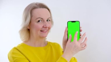 Çekici, çarpıcı, hoş bir kadın, reklam metni için kopyalama alanı olan akıllı telefonu işaret ediyor, yeşil renkli anahtar ekranda, pembe arka planda izole edilmiş, yüksek kaliteli 4K görüntü.