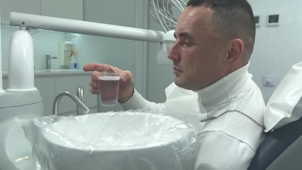 一名男子坐在牙椅正方形的牙齿上 用溶液冲洗口腔 医生为成年人治疗牙齿 — 图库视频影像