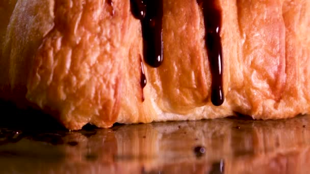 一滴巧克力糖浆热巧克力缓缓流过新鲜烘烤的牛角面包黑色背景巧克力糕点巧克力牛角面包法国甜食配餐 — 图库视频影像