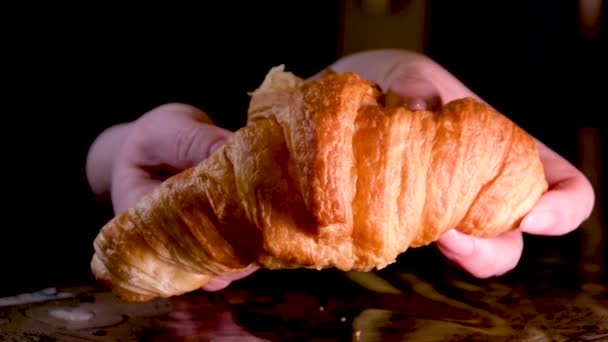 女性の手は 新鮮な暖かいクロワッサンおいしい朝食を破る黒の背景に自家製ケーキテーブルの上に落ちるパン粉は 可視光構造多孔質ペストリーパンデザートです — ストック動画