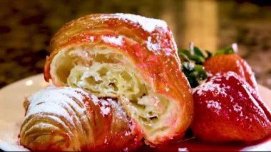 Lezzetli, iştah açıcı, kruvasan, gözenekli hamur işi iki taze çileğin yanına çilek şurubu serpiştirilmiş pudra şekeri serpiştirilmiş.