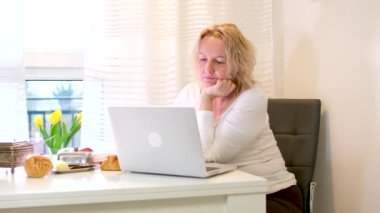 Üşümüş bir sarışının, mutfak masasında doktorla görüntülü konuşma görüntüsü. Belirtilerini tarif ediyor. Yüksek kalite 4k görüntü