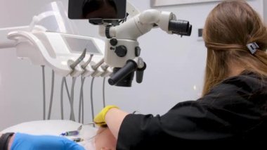 Hastayı incelemek için endodontik dürbünlü mikroskop kullanan maske ve eldiven takan kadın dişçi. Hastaların sağlık hizmetleri kavramının tedavisi için mikroskobu olan modern bir diş kliniği.