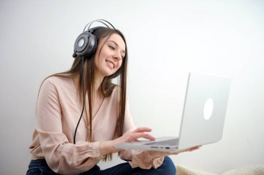 Kulaklıklı neşeli beyaz kadın dizüstü bilgisayarında video görüşmesi yapıyor, Milenyum sandalyesinde oturuyor Webinar 'a katılıyor, uzaktan iletişim kuruyor güzel gülümseme kamerası yavaşça zumluyor.