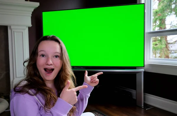 10代の女の子が見事に座っています前に大きな緑のクロマキーテレビモニター広告スペース彼女は熱狂的に指笑う親指アップ賞賛オープン口ワイドすごい誠実な感情を言う — ストック写真