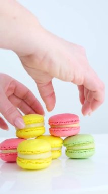 Kız, kurabiyeyi parmağıyla yana doğru sallıyor. Makarna yana yuvarlanıyor. - Sanat. Doğal malzemeler. Çok renkli badem kurabiyeleri. Yemek konsepti. Yüksek kalite renkli lezzetli badem kurabiyeleri dönüyor.