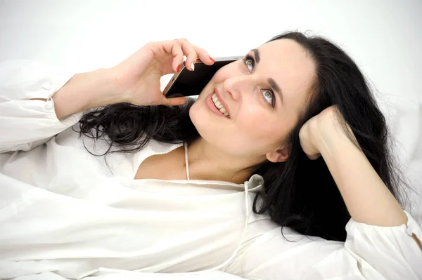 Beyaz Ipek Yatakta Akıllı Telefon Kullanarak Uzanan Güzel Esmer Kadın — Stok fotoğraf