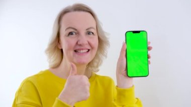 Güzel bir kadın elinde boş ekranın akıllı telefon maketini tutuyor ve beyaz arkaplanda iyi bir işaret gösteriyor