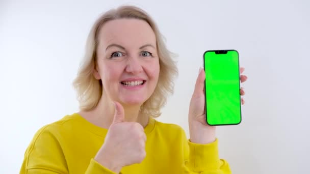 スマートフォンのモックアップを保持し 白い背景にOkサインを示しています美しい女性 — ストック動画