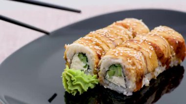 Siyah tabak Kaliforniya 'da suşi. Yılanbalığı siyah yemek çubuklarıyla. Bir kısmı da ön planda wasabi var.