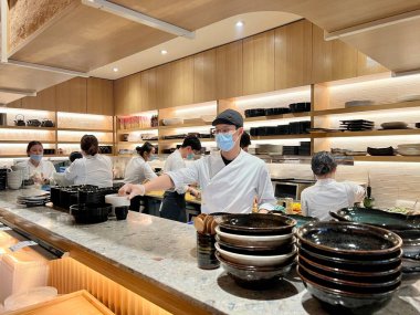 Maskeli ve eldivenli tanınmayan insanlar suşi restoranında Japon yemeği hazırlıyorlar beyaz önlüklü erkekler ve kadınlar temiz giyimli Kanada Vancouver 2023