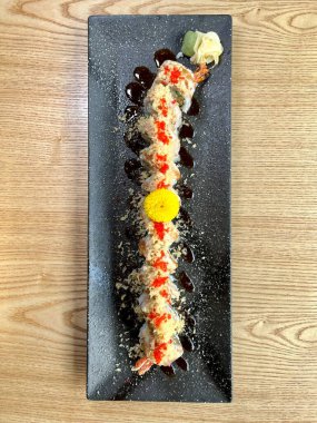 Sarı çiçekle süslenmiş siyah tabakta karides ve yengeçli suşi.