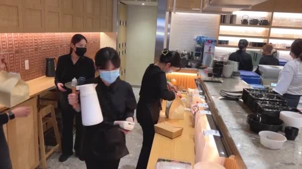 人気の寿司屋多くの料理人やウェイターがテーブルで注文するためにテイクアウトの食べ物を提供します手袋の清潔さのあるマスクですべてを準備します — ストック動画