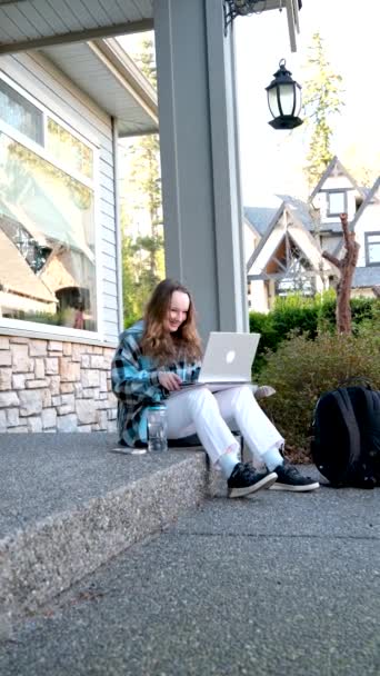 图片中 一个年轻美丽的快乐的女人在户外与笔记本电脑一起工作时 在门廊上美丽的少女微笑 — 图库视频影像