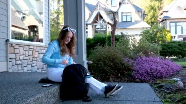Verandada elinde telefonla oturan genç bir kız. Kanada 'da su özel sektöründe beyaz kot pantolonu ve sırt çantası var. Surrey' de iki katlı okul eğitimi var.