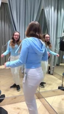 Soyunma odasında dans eden genç kız aynadaki yansımasına bakıp yeni kıyafetler mağazasından alışveriş mağazası alıyor. Gençler kıyafetleri seviyor. Alışveriş merkezinde eğleniyorlar.