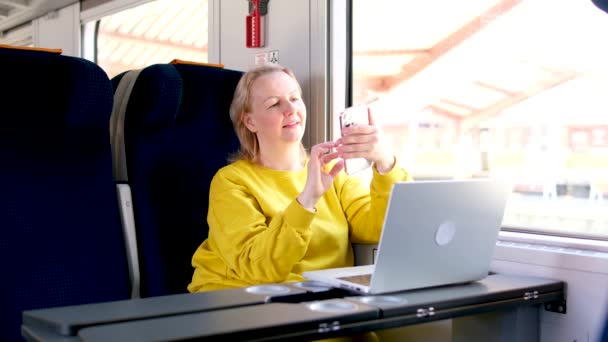 黄色のトラックスーツの女性は テーブルと柔らかい青色の座席を持つIntercityの新しい優れた馬車に旅行中です彼女はノートパソコンをオープン見て置く電話入力テキストメッセージを探しているインターネットWi — ストック動画