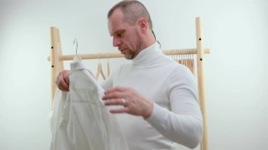Beyaz arka planda iki gömlek tutan bir adam var. Adam hangi gömleği giyeceğine karar veremiyor. Kıyafet seçimine karar verememek. Yüksek kalite 4k görüntü