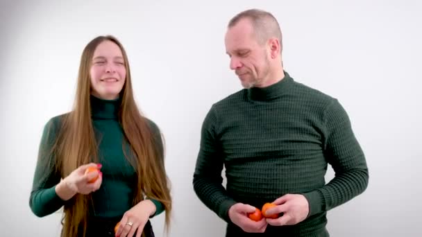 女孩和男人站在彼此的旁边交换橘子女孩扔了一个水果 上面的果子被白色的背景缠住了 男人开始和成熟的 美味的柑橘类水果打交道 — 图库视频影像