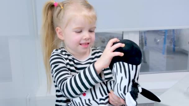 Een Meisje Een Gestreepte Blouse Onderzoekt Haar Tanden Zebra Speelgoed — Stockvideo