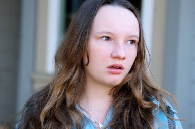 Genç bir kızın hayal kırıklığının yakın plan yüzü. Biraz açık ağızlı. Evin yakınında sağa sola bakıyor.