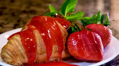 Beyaz tabağa tatlı kruvasanların üzerine çilek şurubu döküyorum. Kahvaltı ya da atıştırmalık lezzetli kruvasanlar. Yüksek kalite 4k görüntü