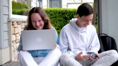 Erkek çocuklar verandada yüksek sesle gülüyorlar sohbet ediyorlar iki telefon el bilgisayarında ev ödevi yapıyorlar spor kıyafetleri giyiyorlar utanç verici spor kıyafetleri giyiyorlar birbirlerine bakıyorlar.