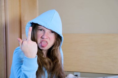 Young latin woman wearing showing middle finger doing fuck you bad expression, provocation and rude attitude. screaming excited girl teenager hood on head stuck out tongue twisted face anger