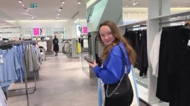 Genç bir kız alışverişe gider. Bir şeyler satın alır kasada ödeme yapar. Farklı giysileri inceler.