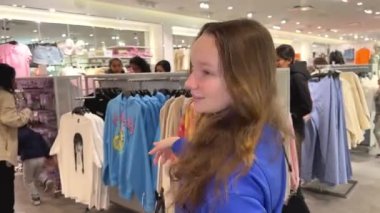 Genç kız kıyafet alışverişi yapıyor ve moda kadını için yeni kıyafet seçiyor. Alışveriş yaparken iyi görünmek istiyor. Gençlik alışveriş sinirleri.