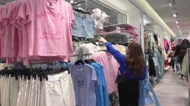 Soyunma odasında dans eden genç kız aynadaki yansımasına bakıp yeni kıyafetler mağazasından alışveriş mağazası alıyor. Gençler kıyafetleri seviyor. Alışveriş merkezinde eğleniyorlar.