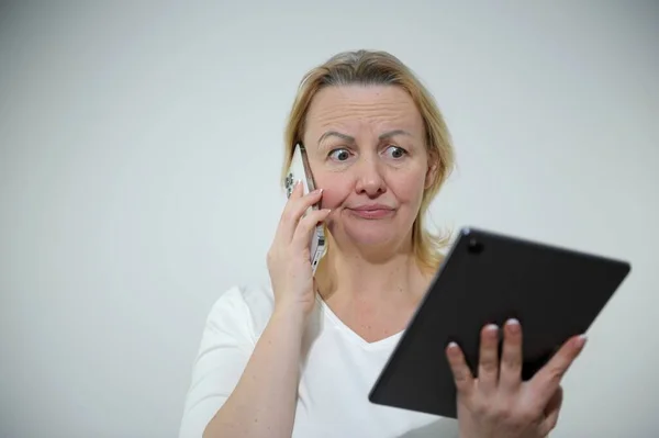 紧张的女企业家在数字平板电脑上边工作边用手机交流 听到坏消息就不高兴 满脸通红 不知道如何让任务坐在桌面上 — 图库照片