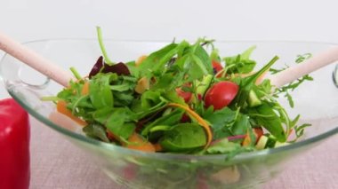 Yakın plan lezzetli yeşil salata ve domates camı derin kase biber tahta kaşıklar beyaz arka plan kamerasında yavaş yavaş diyet gıda vejetaryenliğinin etrafında çekiliyor.