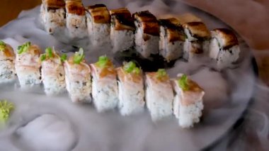 Elleri suşili tabak tutuyordu. Erkek eller suşi teknesini gösteriyor. Kuru buzlu küçük kaseler. Japon yemeği beyaz masada. Yüksek kaliteli FullHD görüntüler