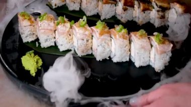 Garson, kuru buz buharı üzerine sushi serpiştiriyor. Siyah taş tabaka California 'nın üzerine yayılmış büyük beyaz duman püskürtücüleri. Kasvetli ton balığıyla servis ediliyor. Vancouver restoranında harika servis ediliyor.