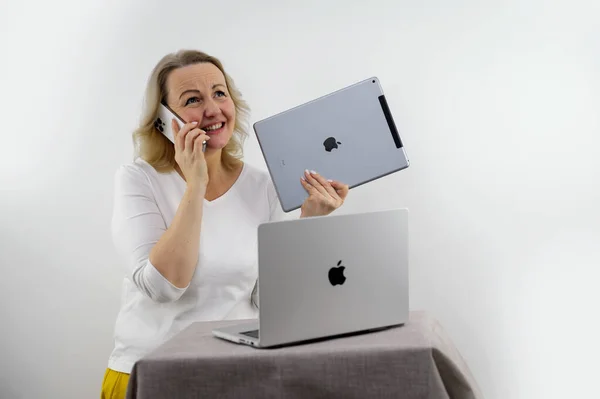 stock image woman received as gift from Apple various gadgets iPad Macbook iPhone 13 Pro Max on white background middle-aged blonde dancing rejoices waving space for text newest technologies happiness win victory