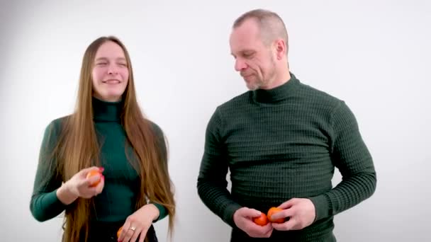 女の子と男はお互いの横に立っている交換みかんの女の子は白い背景にキャッチトップ1を投げました男は熟したおいしい柑橘系の果物の関係でジャグリングを開始します — ストック動画