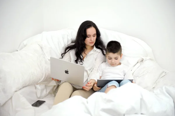 husband wife in bed with little son looking at tablet cartoon interesting game pictures laughing talking communication real people at home love life happy family with tablet pc in bed at home