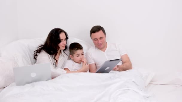 丈夫的妻子和小儿子在床上看着平板卡通片有趣的游戏画面笑着与人交流真正的人在家里爱着生活快乐的家庭生活快乐的人白种人背景 — 图库视频影像