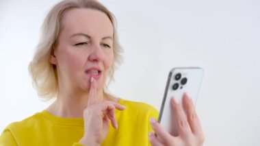 Güzel bir kadın beyaz cep telefonu kullanıyor, dokunuyor ve ekrana bakıyor, gri arka plan. Yüksek kalite 4k görüntü