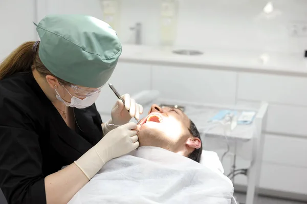 Female Dentist Green Hat Black Clothes Treats Male Patient Operation — Stock Photo, Image