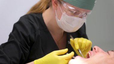 Hasta ağzını retraktör ve dişçiyle kapatın. Anestezi yapın ve tükürüğünüzü emici tüple temizleyin. Dişçi koltuğunda tedavi gören beyaz bir erkek hasta. 