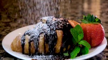 Beyaz tabakta nane şekeri üzerine serpiştirilmiş kruvasan üzerine koyu çikolata ve evde yapılan lezzetli Fransız restoranında servis edilen mermer masa tatlısı.