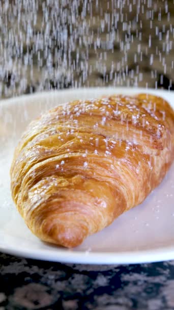 閉じるおいしい食欲をそそる新鮮なカリカリのクロワッサン大理石のテーブルの上に粉砂糖を振りかけた白いプレートおいしい食べ物ランチスナック多孔質構造ベーキングダイエット場所広告メニューフランスの朝食 — ストック動画