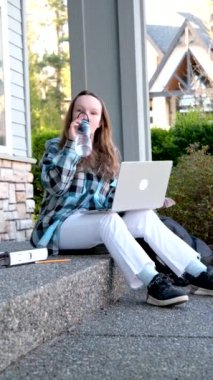 Genç kız sundurmada oturup dizüstü bilgisayarın yanında su içiyor arkadaşlarıyla ev ödevi yapıyor dinleniyor, sınıf arkadaşlarıyla gülüyor internette özel sektör Surrey 'i izole etmeyi öğreniyor.