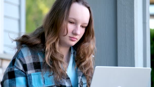 十代の女の子座っています前にラップトップの時計の映画ややって宿題をオンライン研究として仕事を探しています十代の若者たち楽しみます側Shrugs入札美しいです若い女性ヨーロッパの顔白い肌 — ストック動画