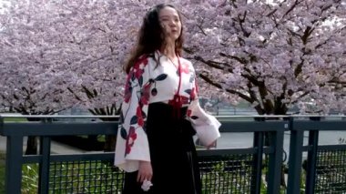 Gezgin kız, Vancouver 'da, Kanadalı kiraz çiçeklerinin arka planında saçlarını tarayan güzel Doğulu genç bir kız, demir köprünün üzerinde, sakura çiçek bahçesinde yürüyor.