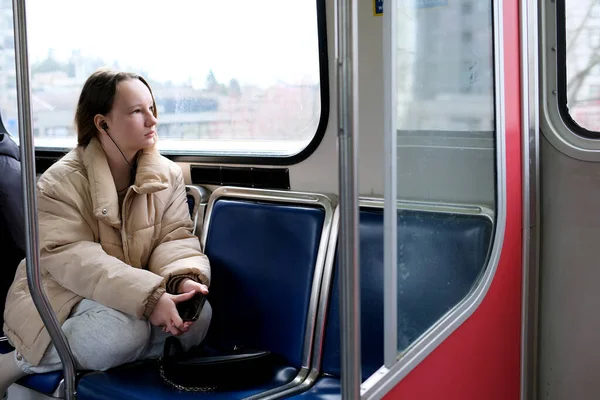 Teen girl looking at window of metro train. Cute woman travel by sky train Concept of public transport and urban journey vancouver canada listen to music on headphones go home to study