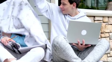 Gençler verandada oturmuş kızların kafalarına ekose takıyor ders almak için dizüstü bilgisayar klasörüne gülüyor okula gidiyor açık spor giyim gençlik iletişimi