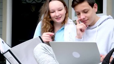 Ergen, evden birlikte online eğitim almak için dizüstü bilgisayar ve tablet kullanıyor. Karantina konsepti verandada oturup kulağına fısıldıyor. Ev ödevlerini yaparken büyük beyaz klasörde eğlenmene bak.